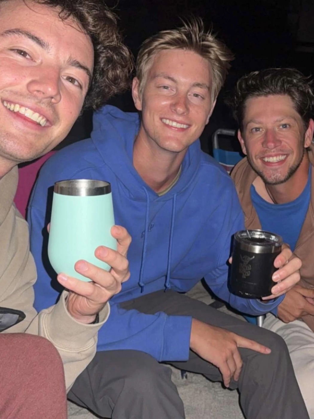 Kadin and two friends smiling at night, raising insulated tumblers