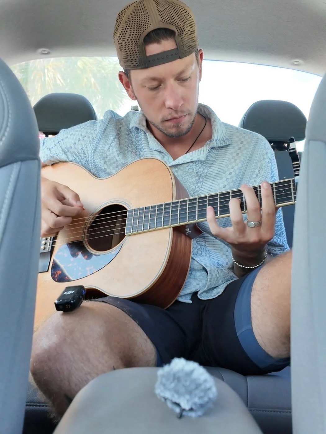 Kadin playing an acoustic guitar in the back seat of a car