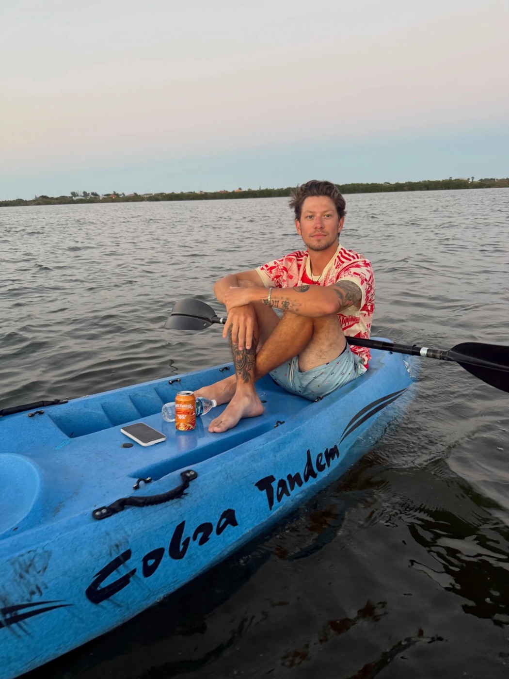 Kadin relaxing barefoot in a blue tandem kayak on calm Florida water at golden hour